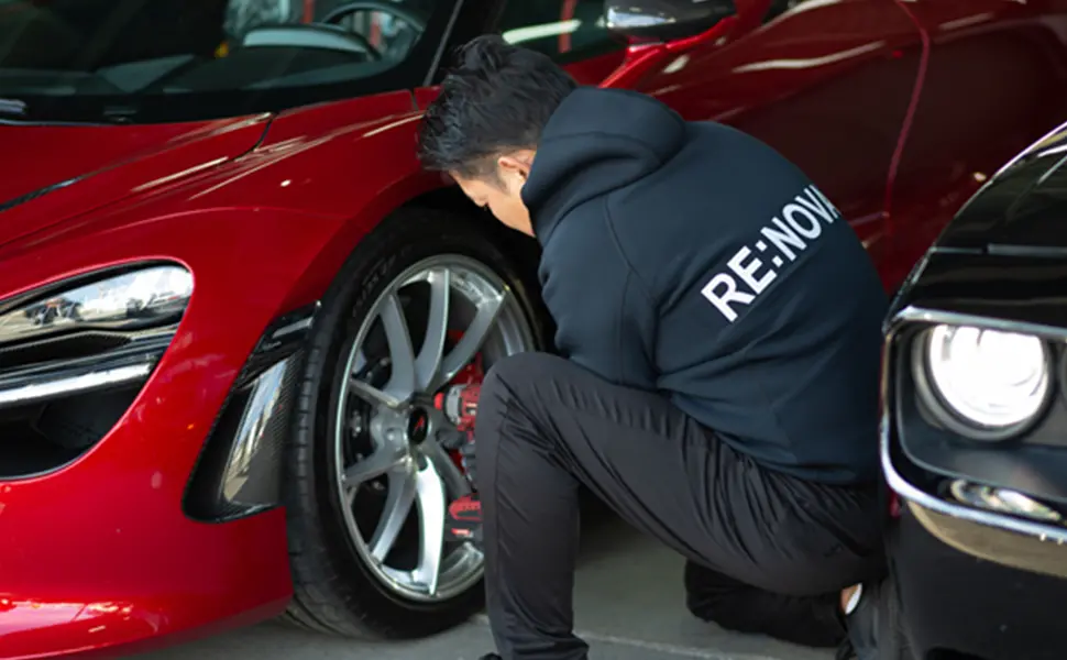 赤いスポーツカーのホイール付近を点検または整備する男性