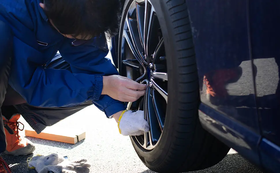 青いジャケットを着た人物が車のホイールナットを工具で締めている
