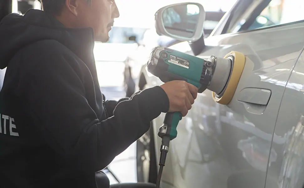 電動ポリッシャーで白い車のボディを磨く作業員