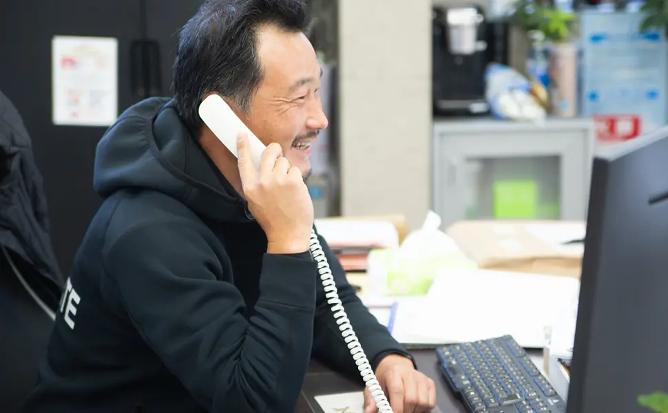 デスクで電話を取りながら笑顔で会話する男性