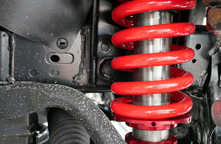 自動車の足回りに取り付けられた鮮やかな赤色のサスペンションスプリングがクローズアップで写されている