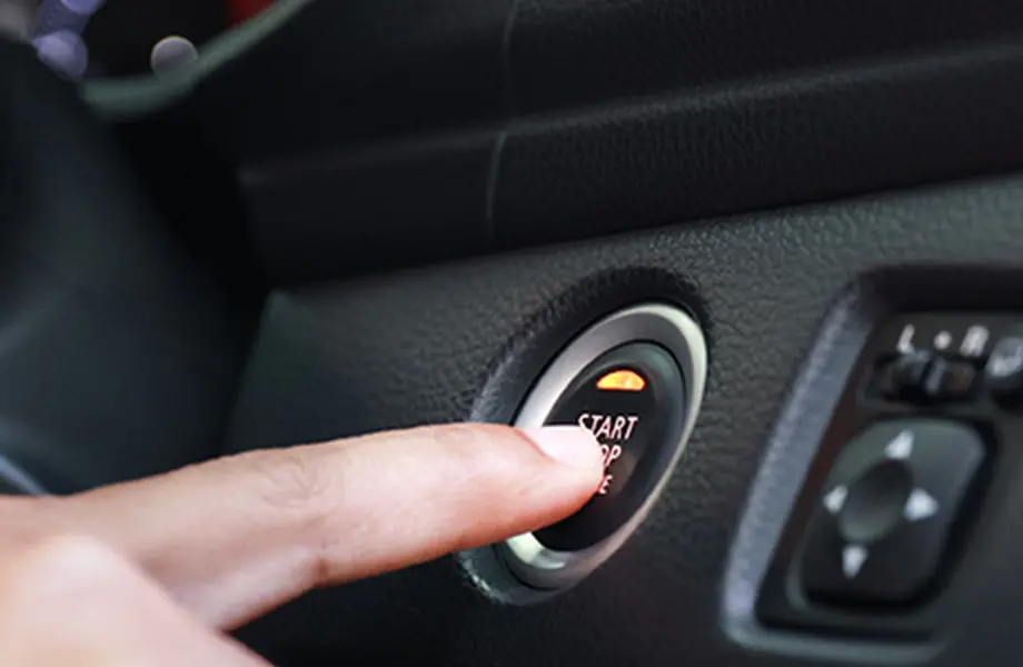 車のエンジンスタートボタンを押す手元、押下後に点灯するライトが映っている