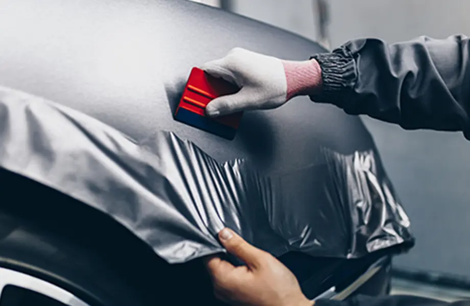 車のボディにラッピングフィルムを貼っている作業の様子、ヘラで空気を抜いている