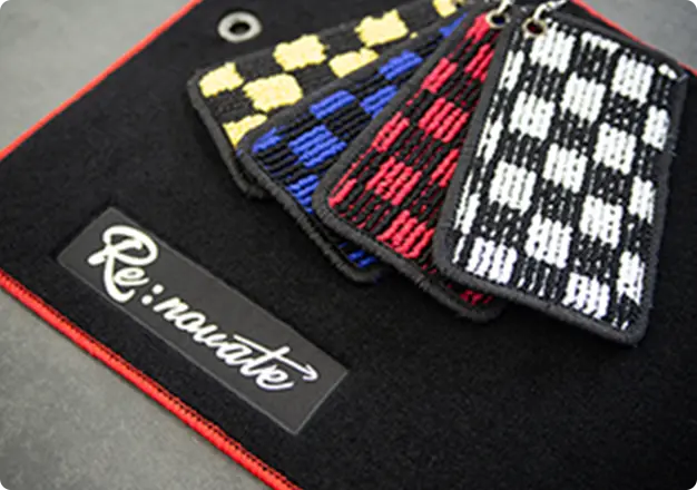 Re:novateロゴ入りのカーマットとチェック柄キーホルダーが並んでいる様子