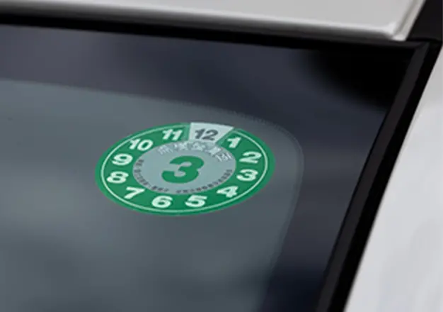 車のフロントガラスに貼られた緑色の車検ステッカーが写っており、有効期限が「3月」であることを示している。