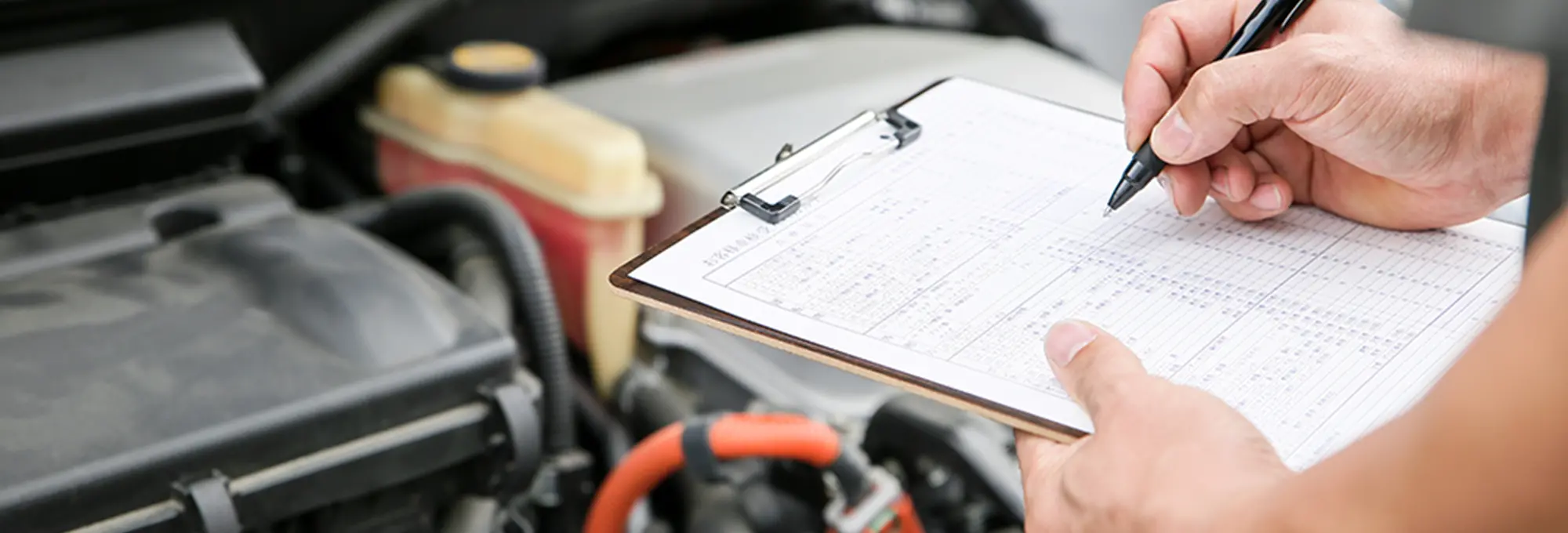 車のボンネット内を前にして整備士が点検チェックシートに記入している様子