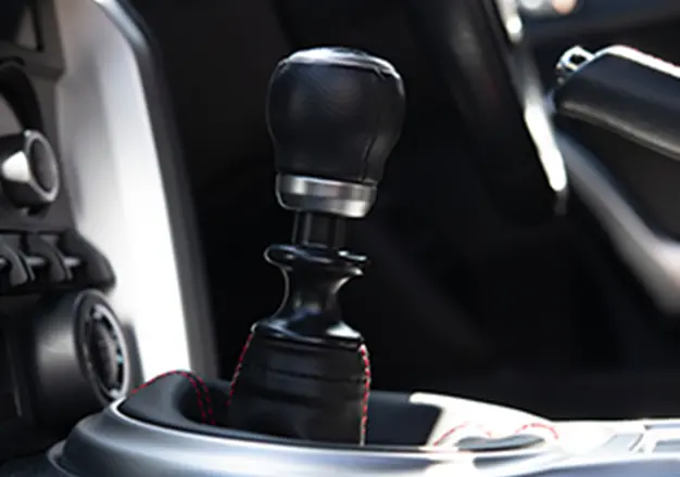 車のマニュアルシフトレバーのクローズアップ、黒革と赤いステッチが印象的