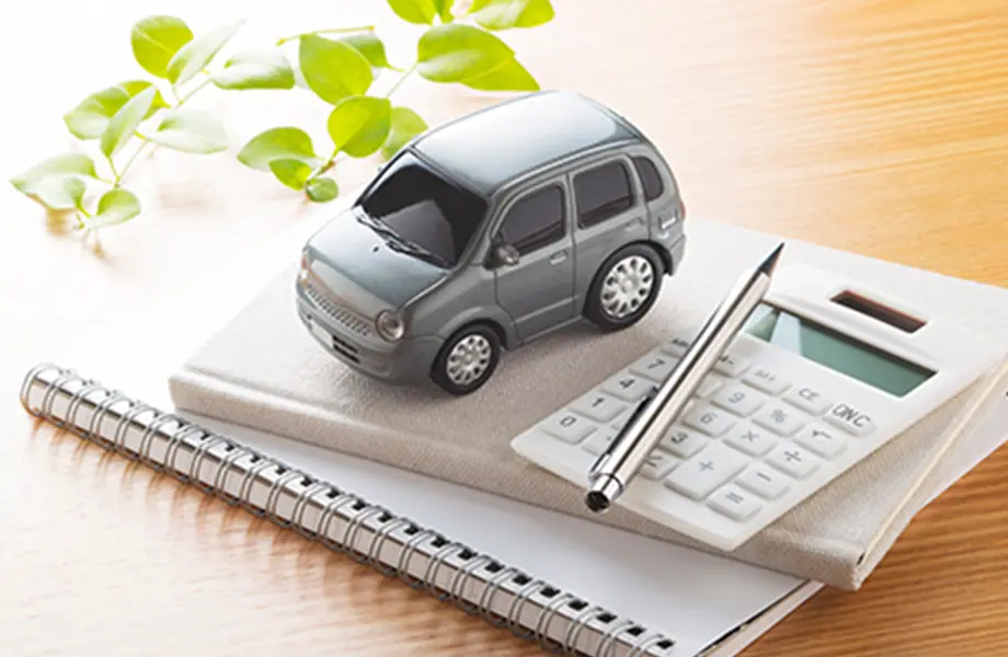 車の模型と電卓、ノート、ペンが置かれたデスク上の風景