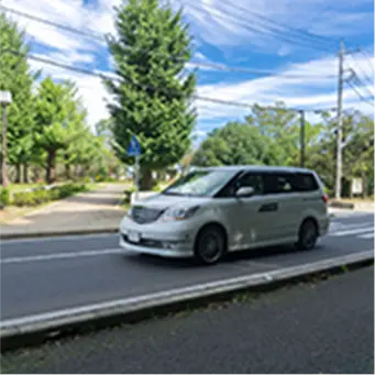 両側に木々が並ぶ道路を走行中の白いワンボックスカーの風景