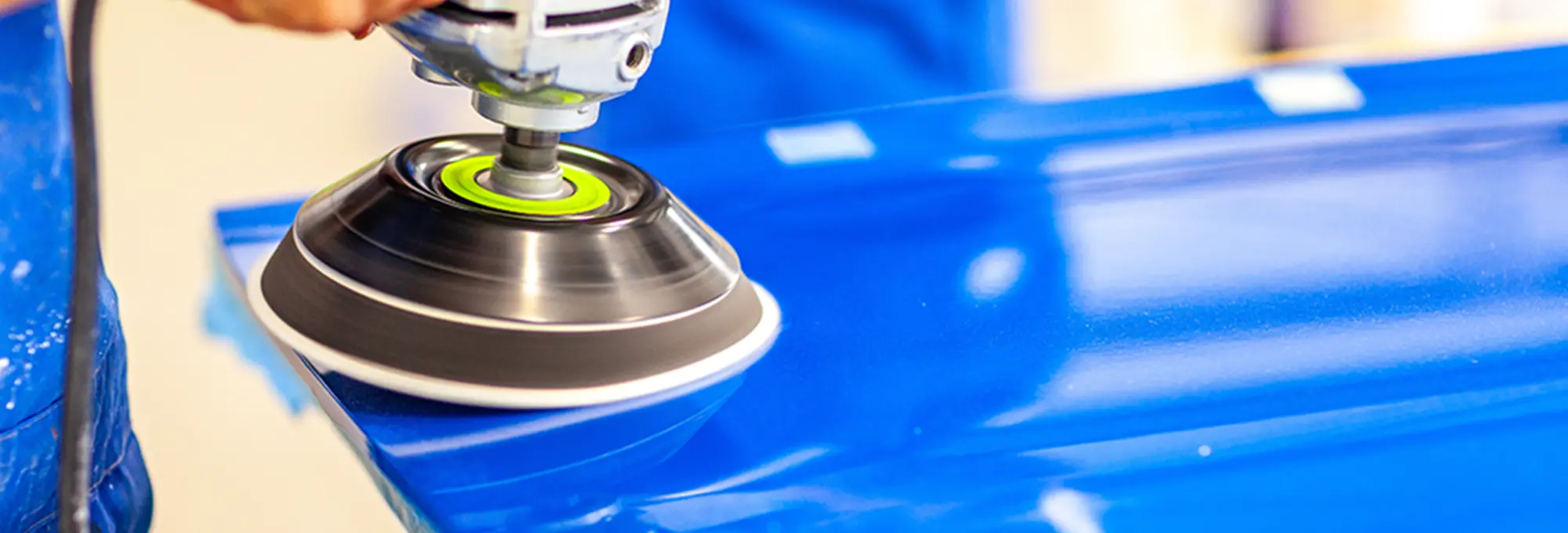 青い車のボディにポリッシャーをかけている作業の様子、磨き作業をしている手元