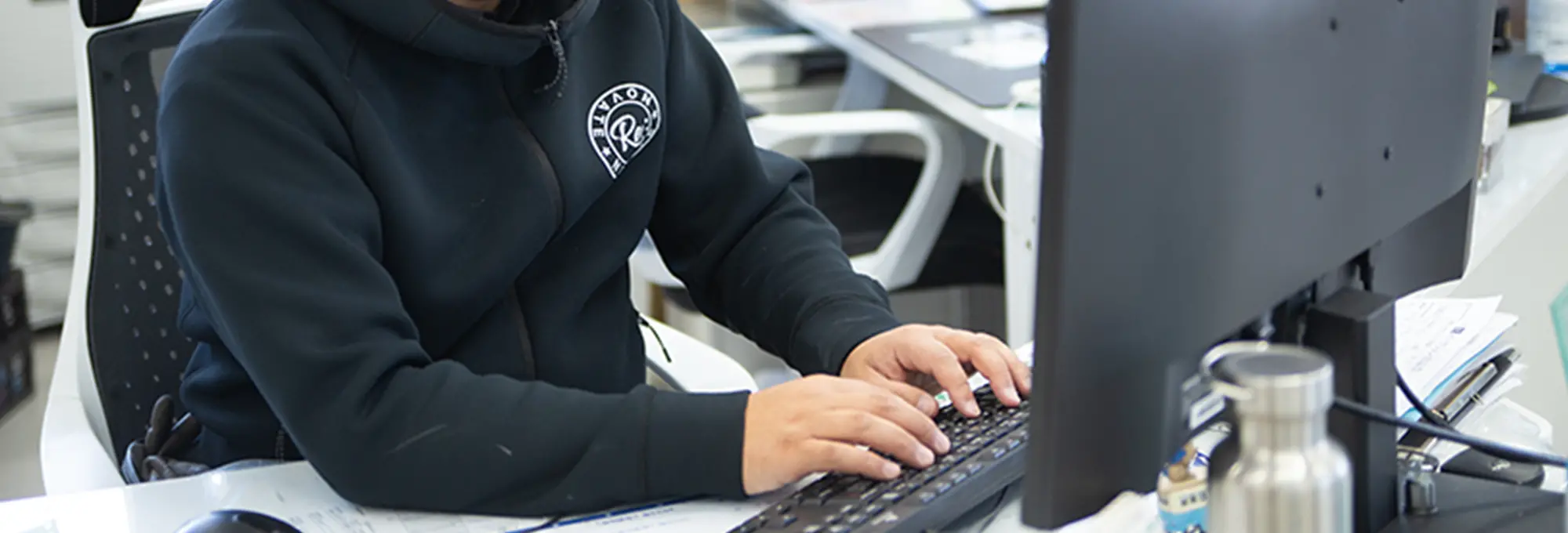 デスクでパソコンを操作するフーディー姿のスタッフの手元